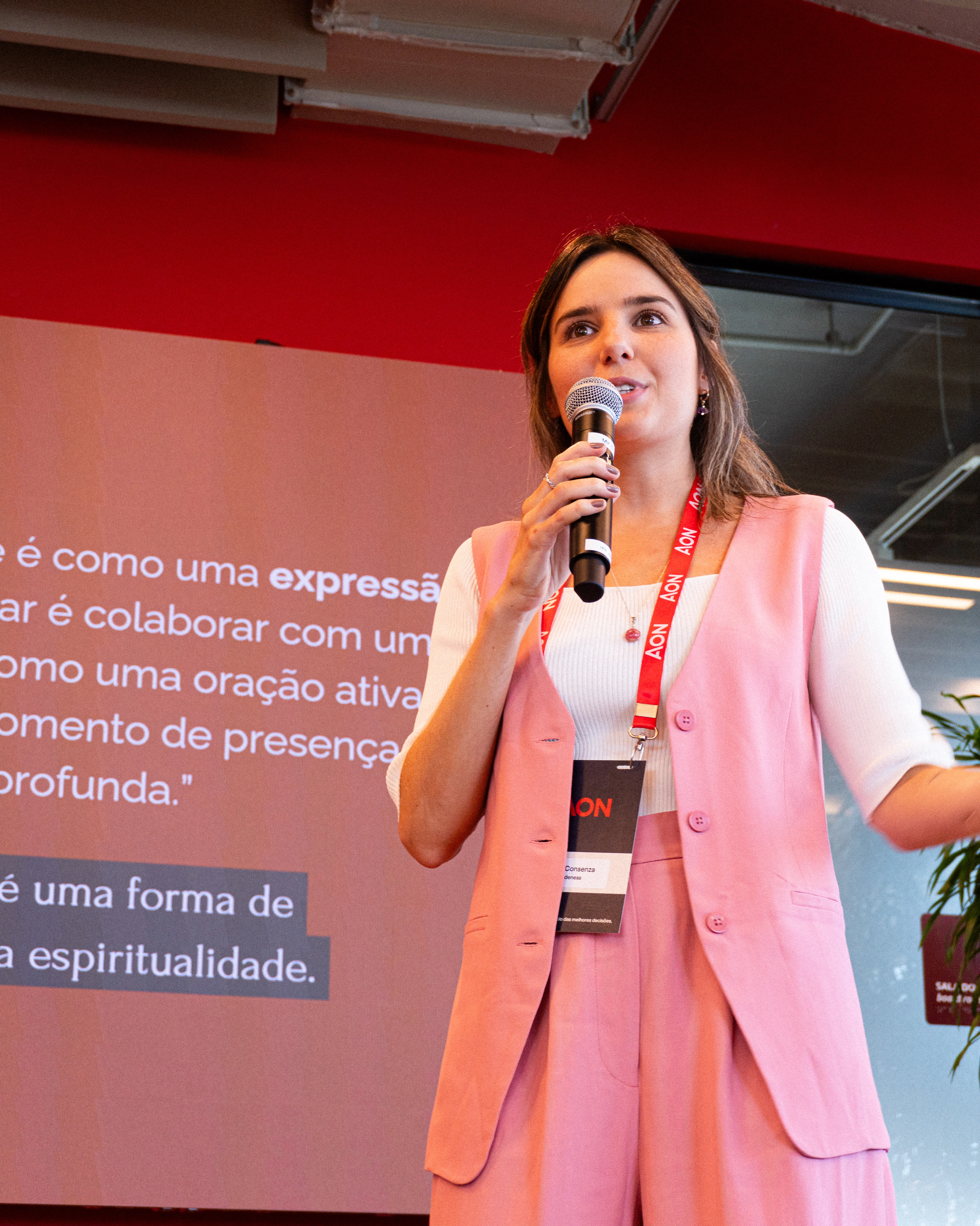 Bruna está sorrindo e olhando diretamente para a câmera, segurando o encarte da Oficina de Colagens e Processos Criativos.